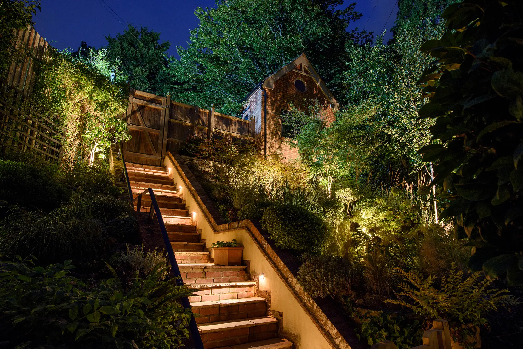 Brick garden steps rising through planting, lit by recessed step lights and border uplights